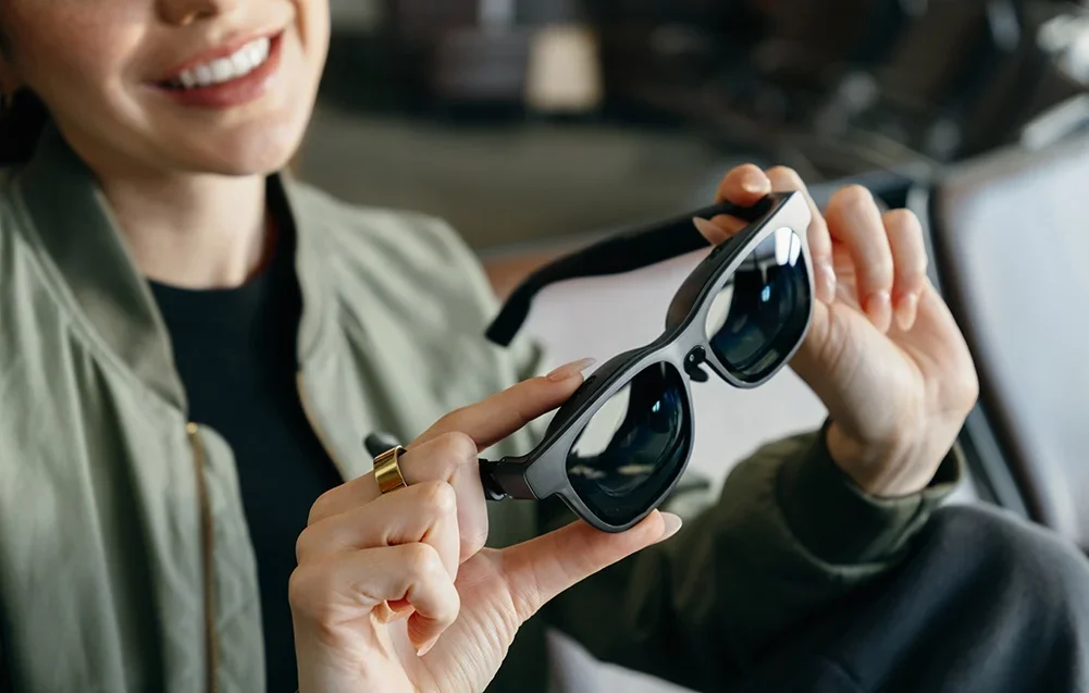 Besišypsanti moteris laiko rankose juodus išplėstinės realybės akinius