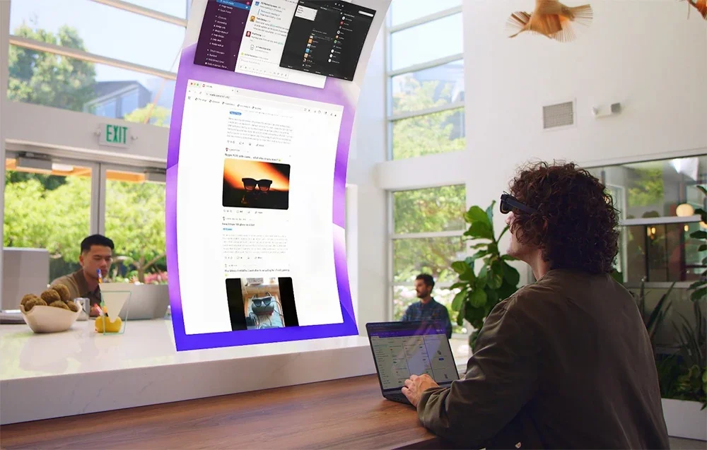 Žmogus sėdi šviesiame kambaryje su nešiojamuoju kompiuteriu ir naudojasi XR akiniais