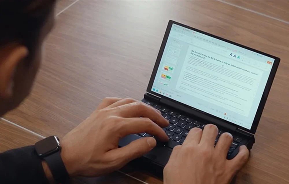 Watch hands typing on a laptop with an open text document on a wooden desk