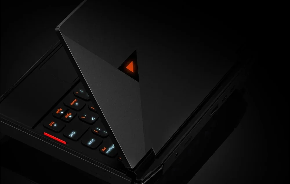 Close-up of black gaming console with orange logo and backlit keyboard against dark background